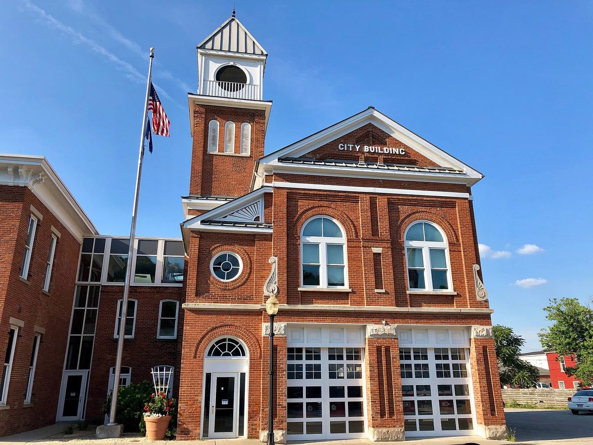 A red-brick city hall with a clock tower and flags under a blue sky